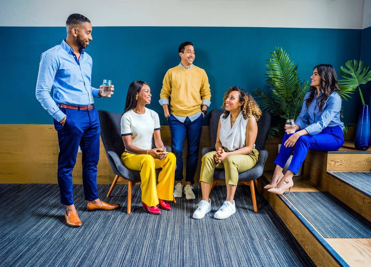 A group of four happy people wearing jeans and trousers, smiling with their legs crossed.